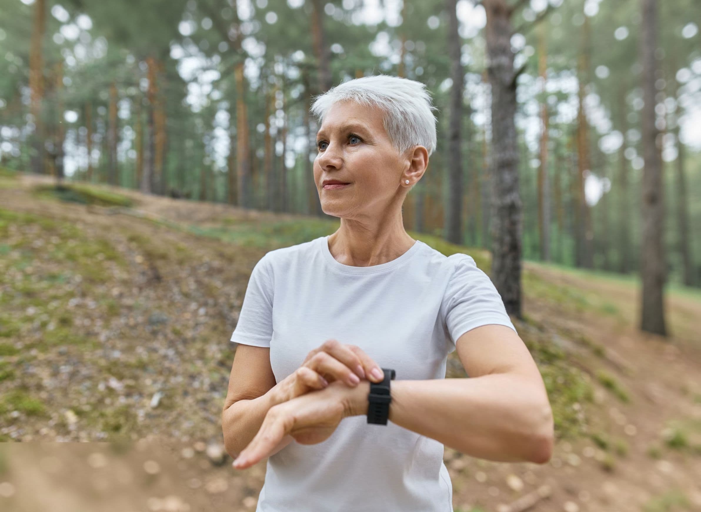 Active senior woman checking fitness tracker during an outdoor walk in the forest