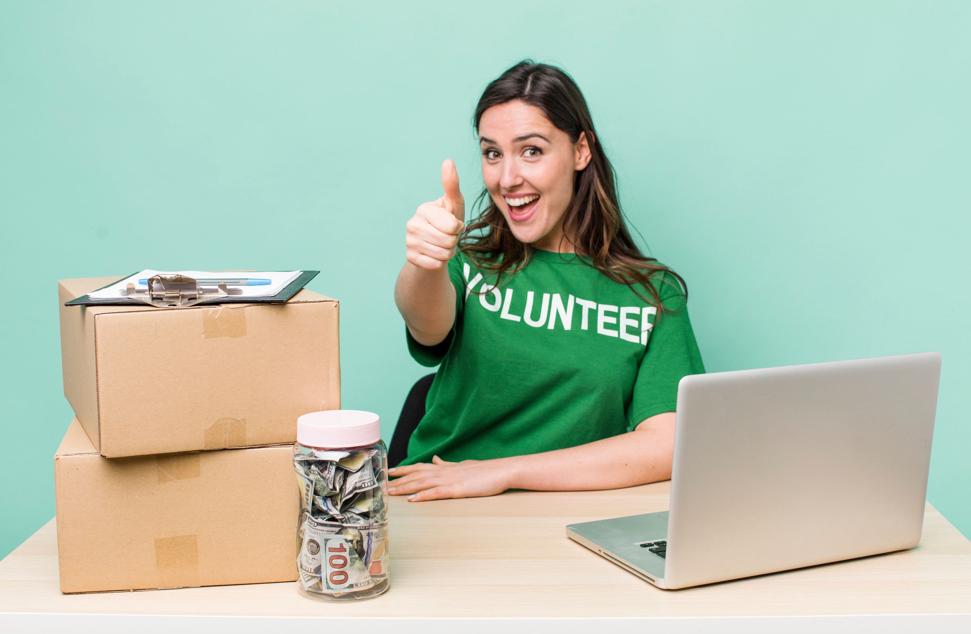 Smiling volunteer giving a thumbs up while organizing donation boxes and fundraising activities, representing community support, charitable giving, and social impact